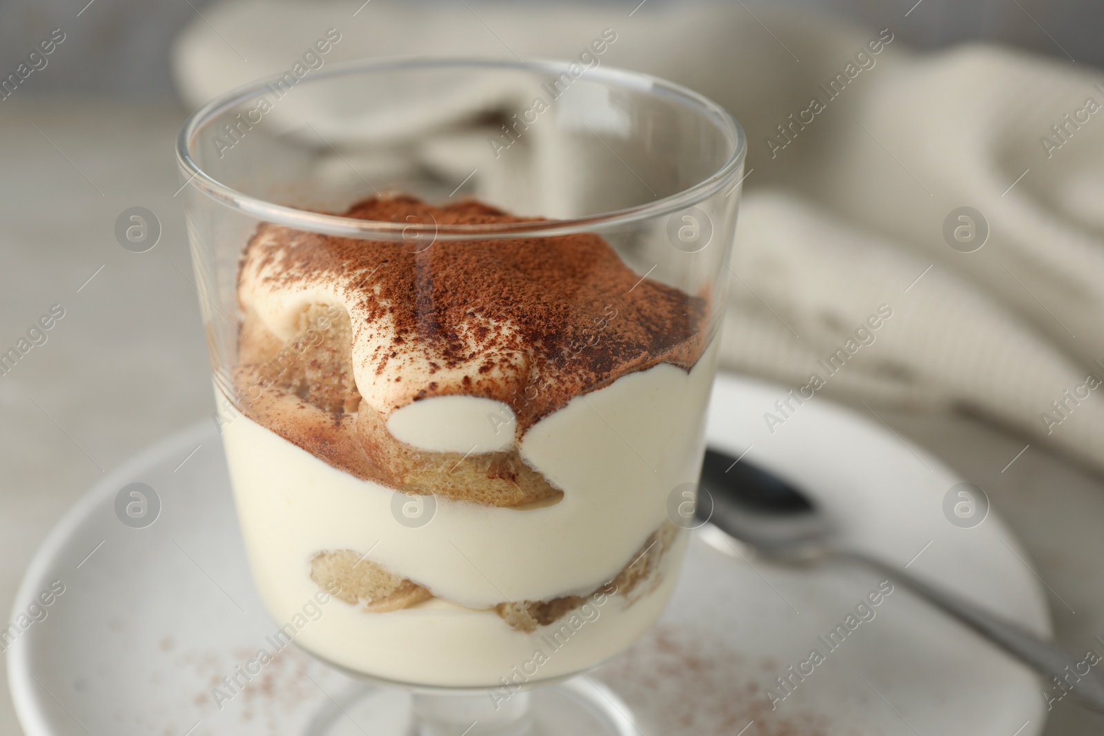 Photo of Delicious tiramisu in glass on light table, closeup