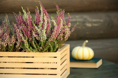 Photo of Beautiful heather flowers in crate on table near wooden wall, selective focus. Space for text