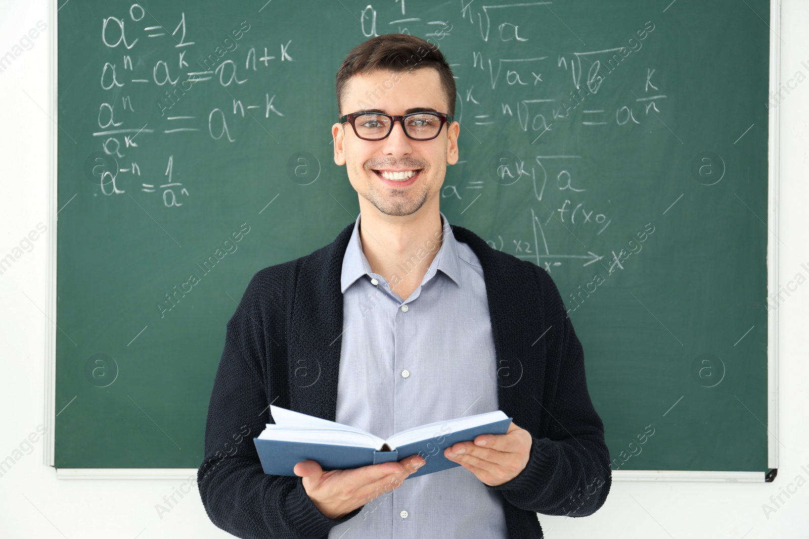 Photo of Young male teacher with book standing in classroom