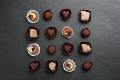 Photo of Different delicious chocolate candies on black table, flat lay