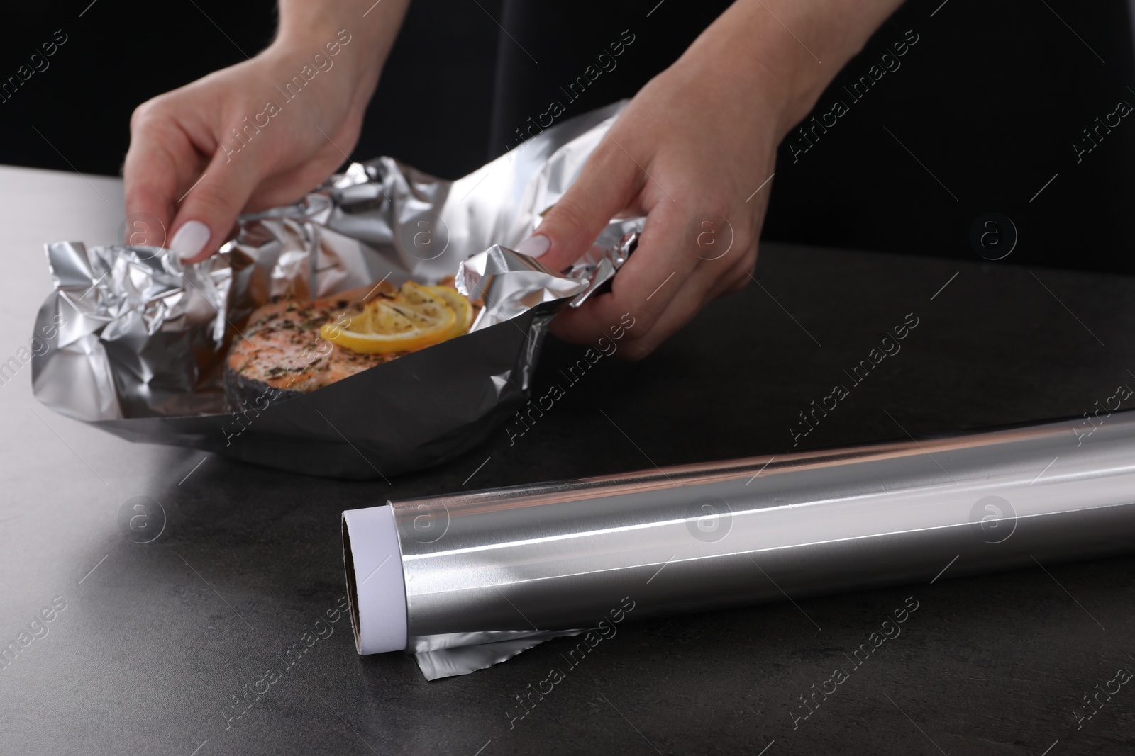 Photo of Aluminum foil and woman with tasty salmon at grey textured table, closeup