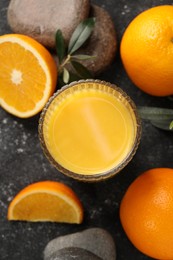 Photo of Tasty fresh oranges, juice, stones and leaves on black table, flat lay