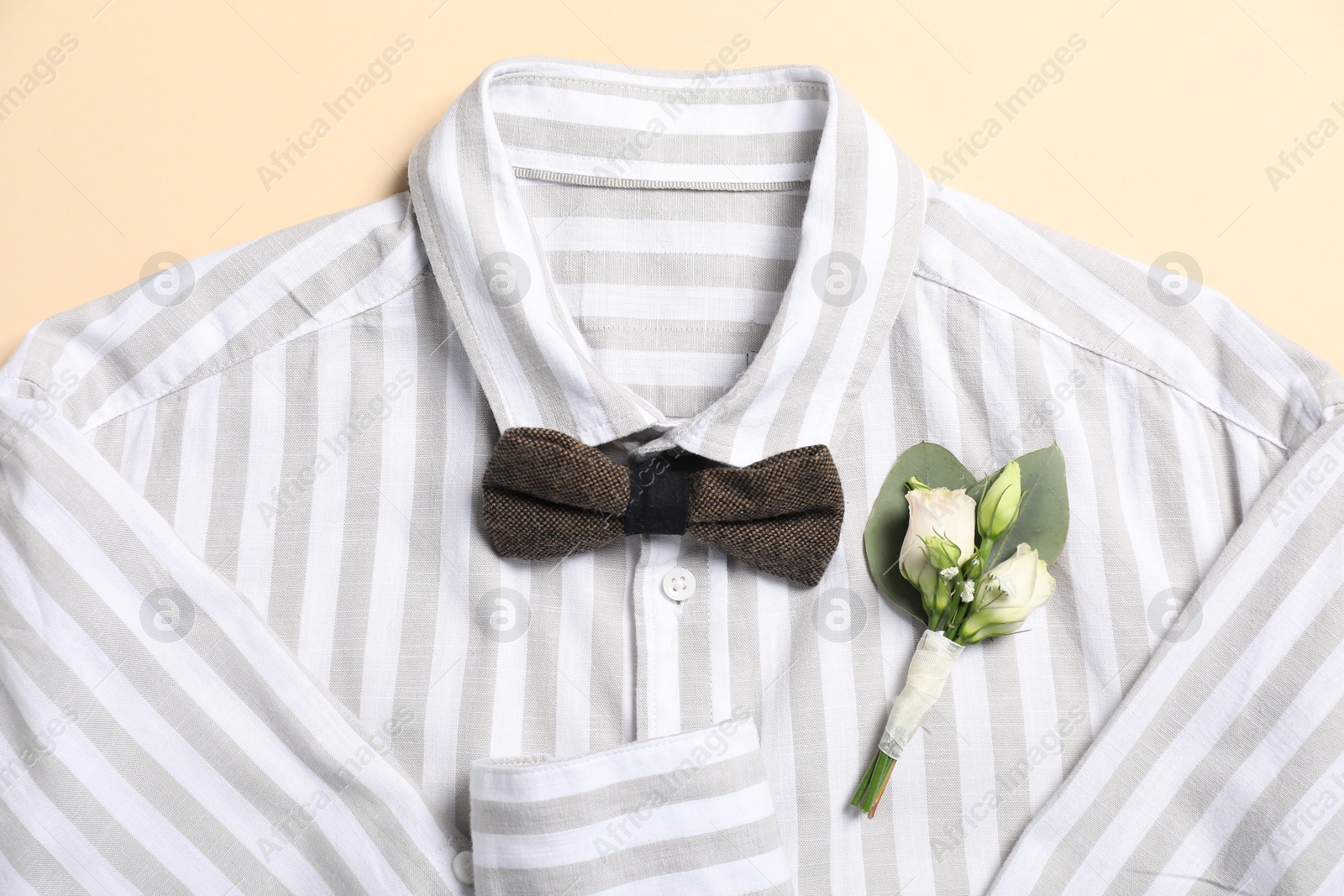 Photo of Wedding stuff. Stylish boutonniere, shirt and bow tie on beige background, top view