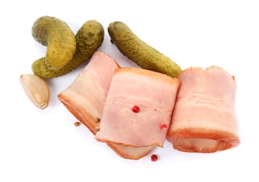 Photo of Slices of delicious smoked bacon with peppercorns, garlic and pickled cucumbers on white background, top view