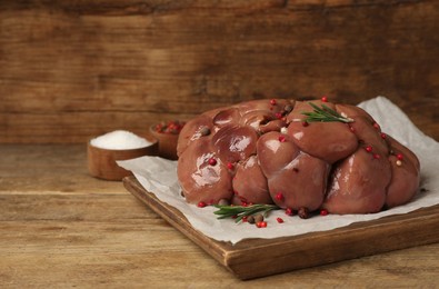 Photo of Fresh raw kidney meat with spices and rosemary on wooden table, space for text