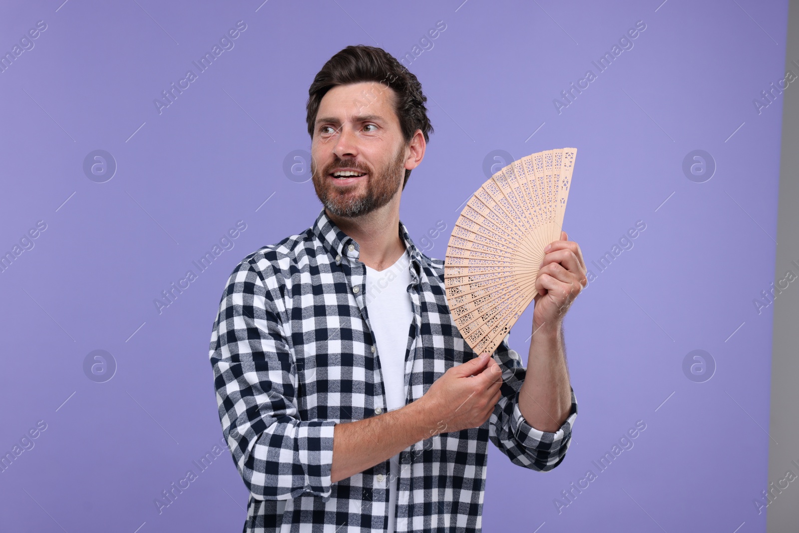 Photo of Happy man holding hand fan on purple background