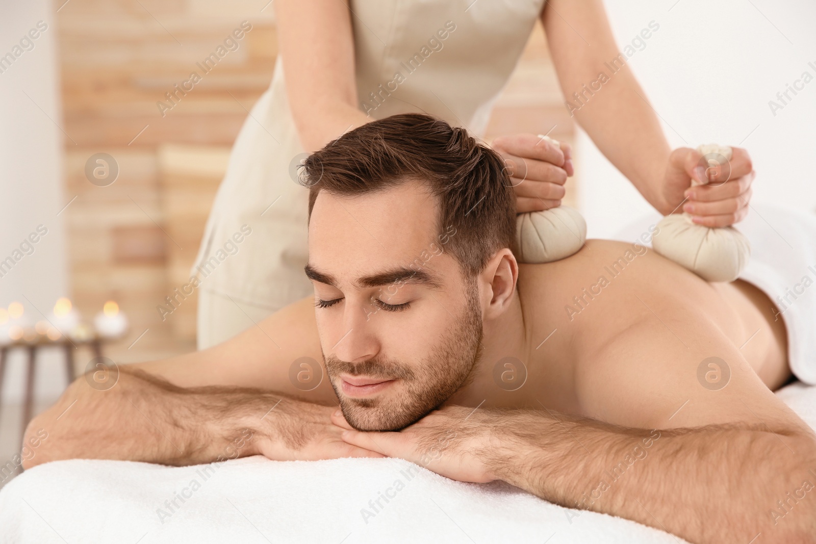 Photo of Handsome man receiving herbal bag massage in spa salon