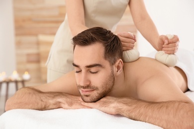 Handsome man receiving herbal bag massage in spa salon