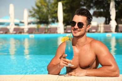 Young man with cocktail in pool on sunny day