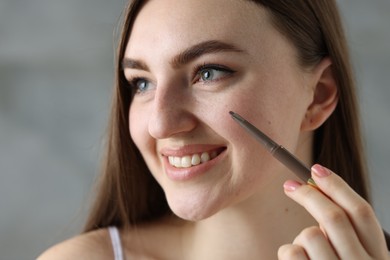 Photo of Smiling woman drawing freckles with pen indoors, closeup