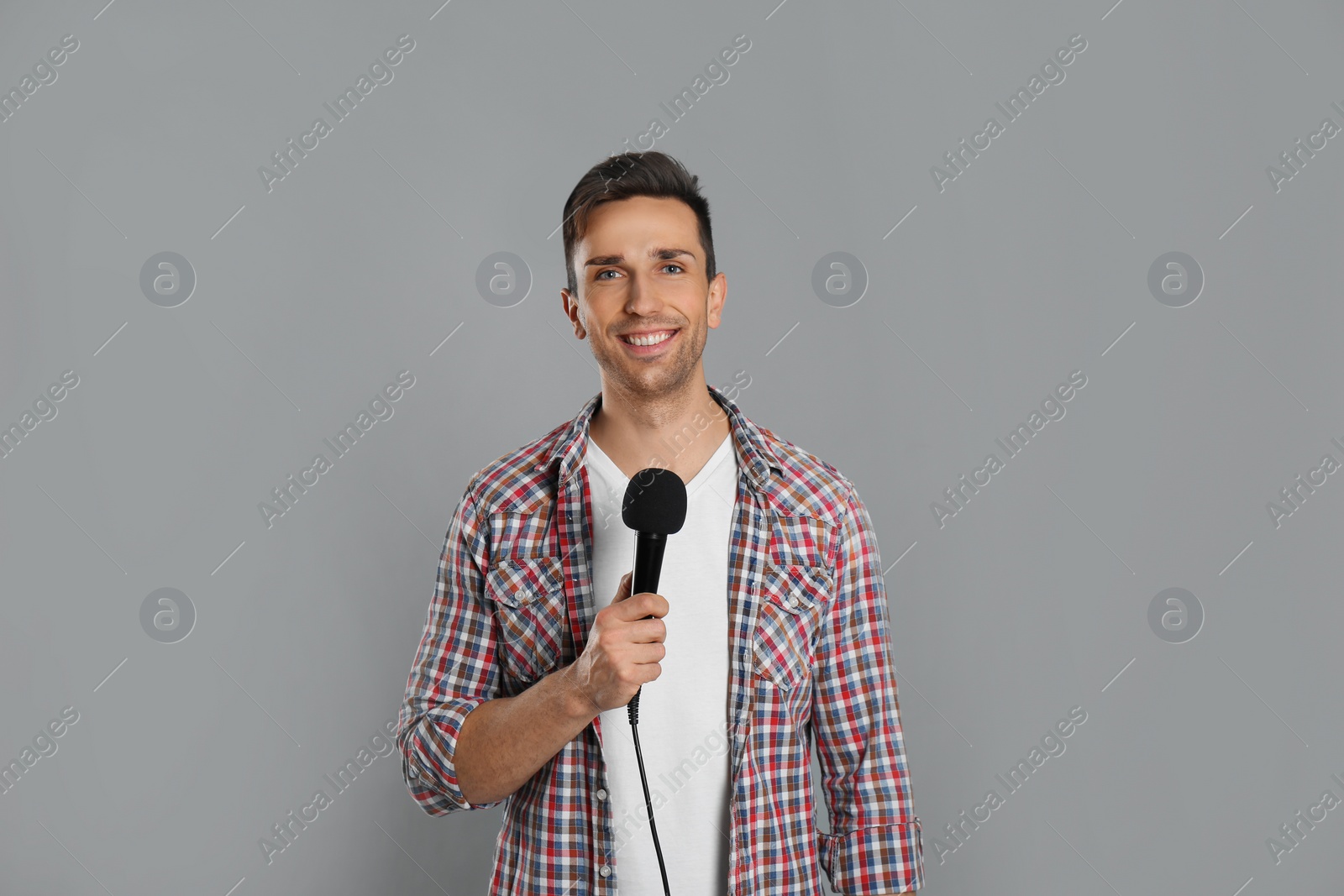 Photo of Young male journalist with microphone on grey background