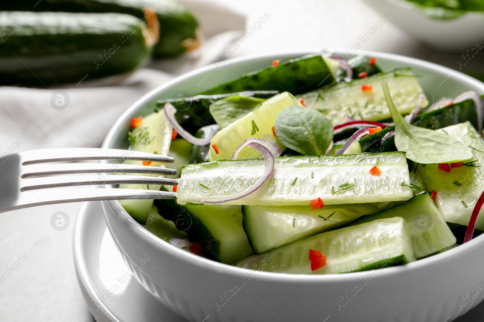 Photo of Delicious cucumber salad with onion and spinach in bowl on table, closeup