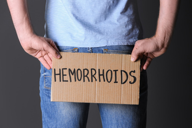 Man holding carton sign with word HEMORRHOIDS on black background, closeup