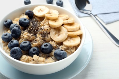 Photo of Tasty oatmeal with banana, blueberries and chia seeds served in bowl on white wooden table, closeup
