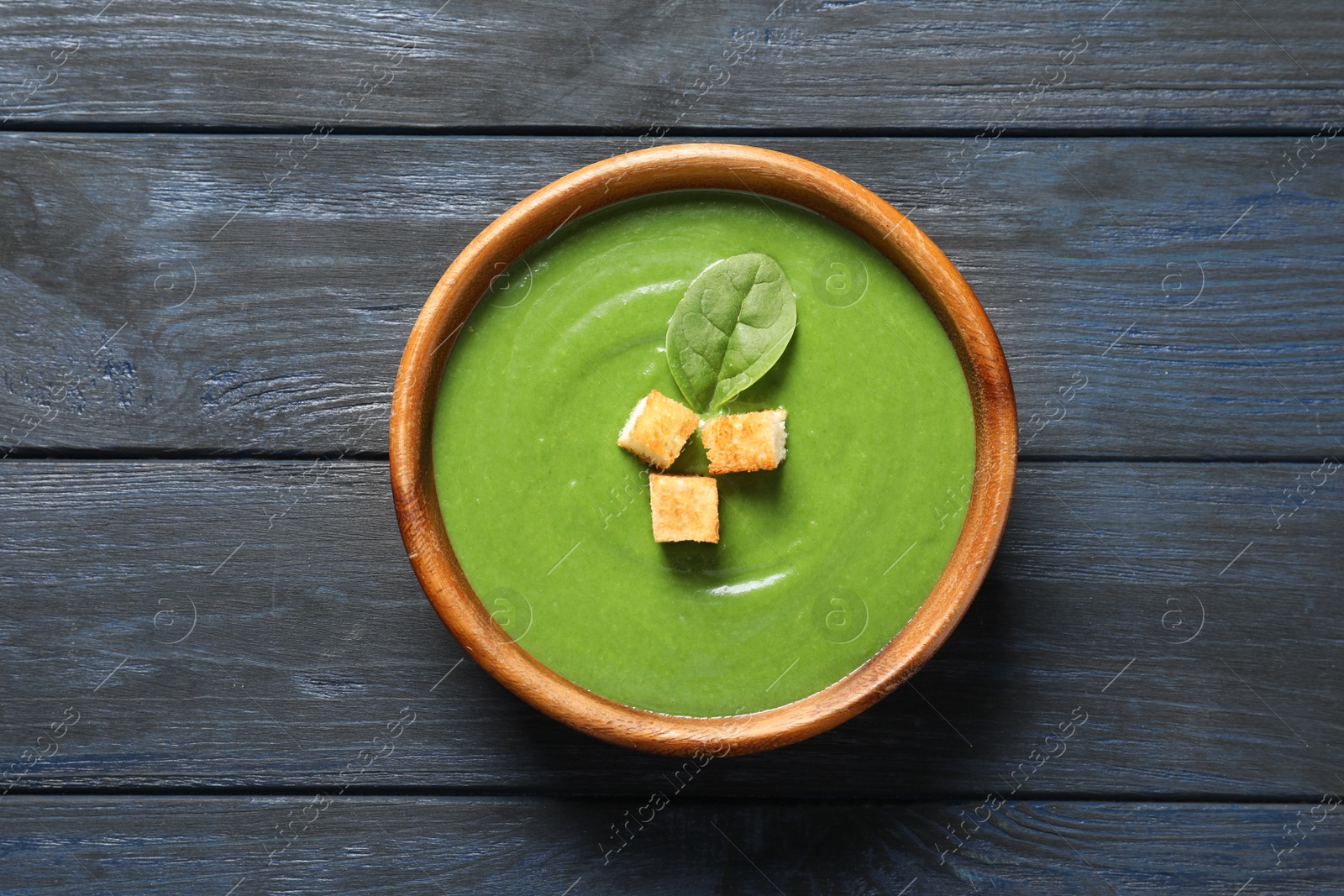 Photo of Fresh vegetable detox soup made of spinach with croutons in dish on wooden background, top view