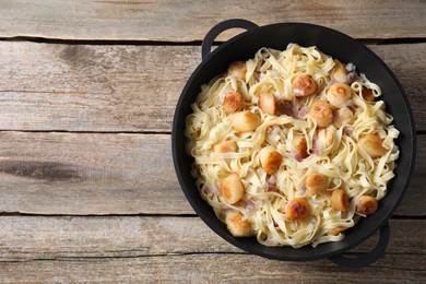 Photo of Delicious scallop pasta with onion in pan on wooden table, top view. Space for text