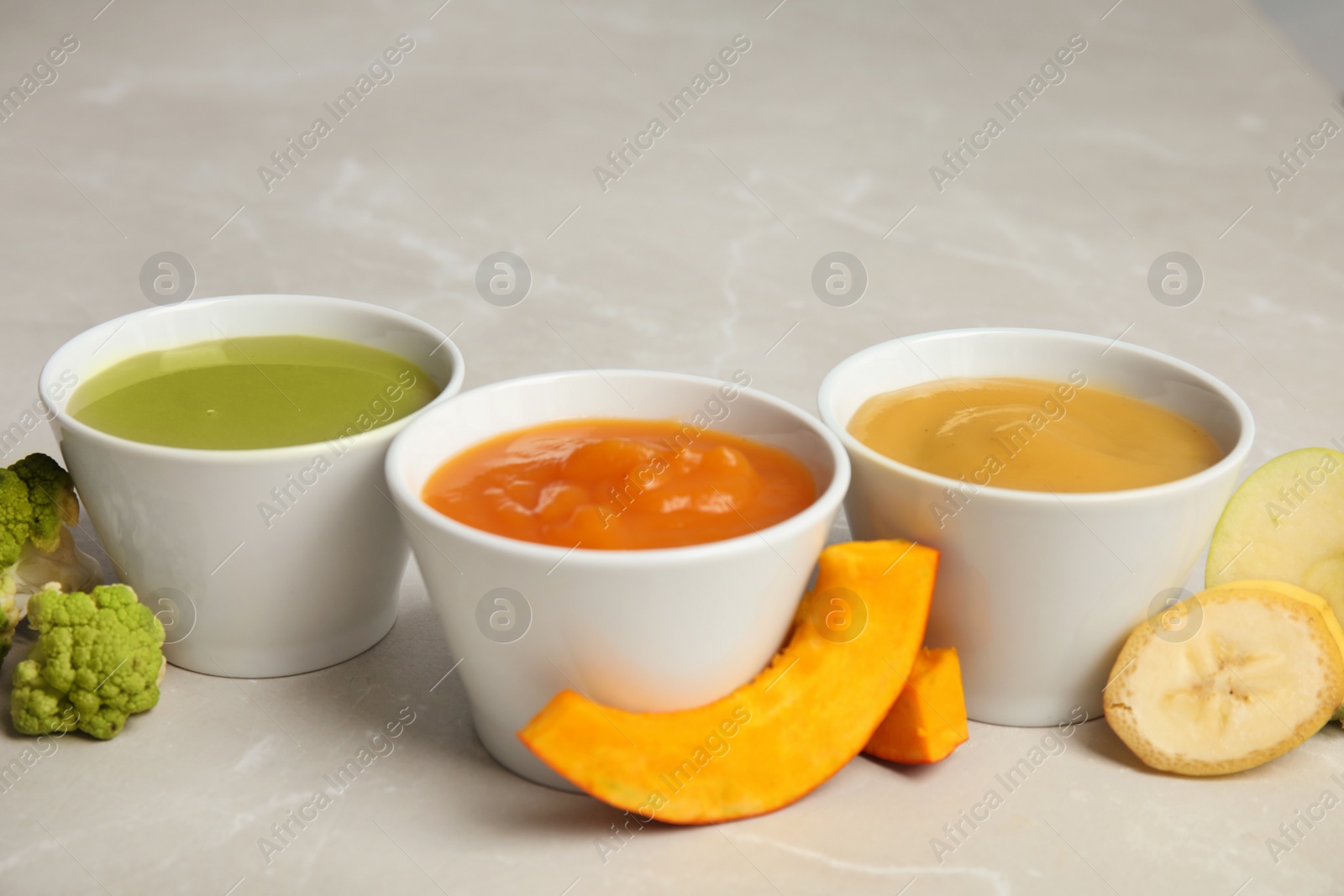 Photo of Bowls with different baby food on gray background