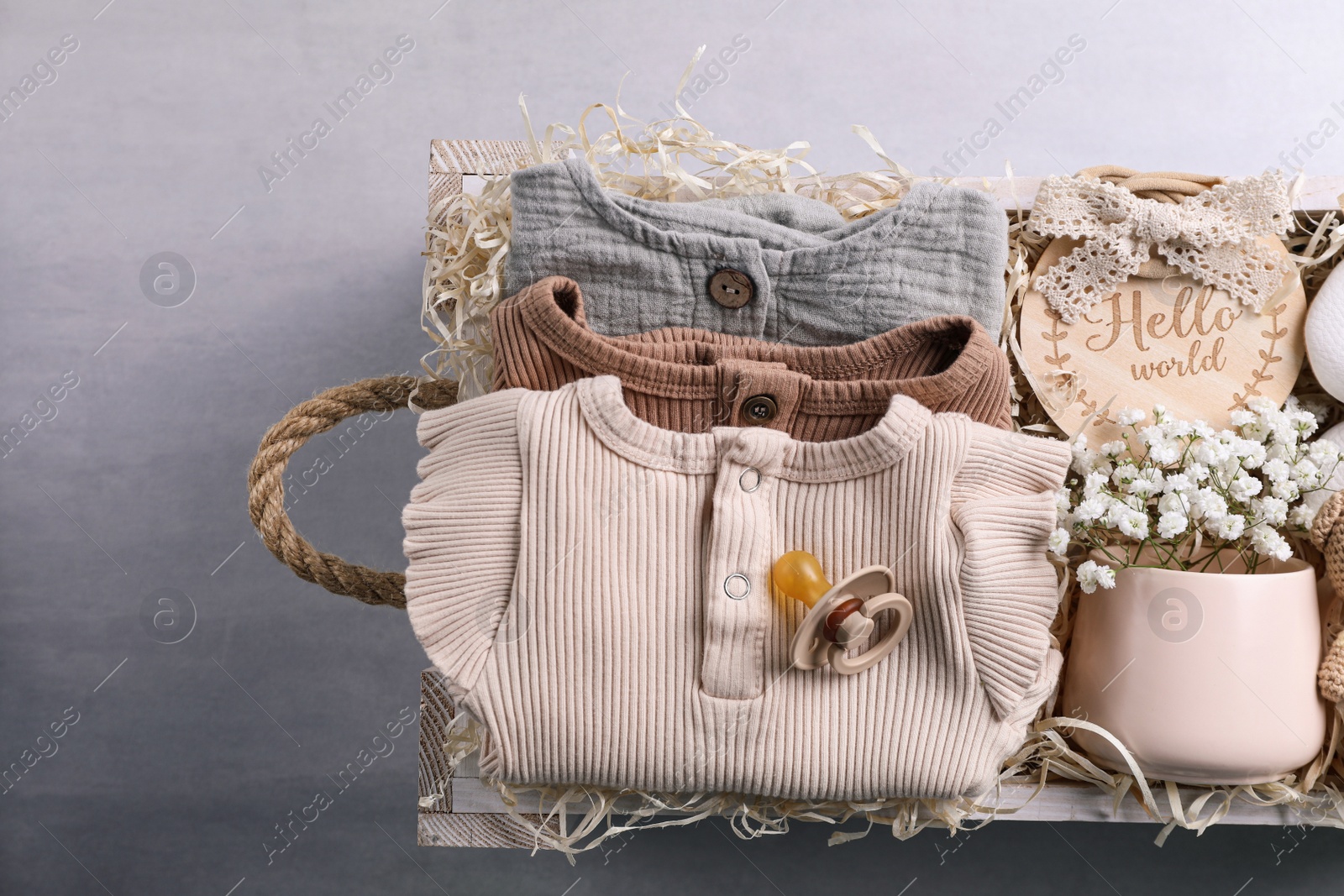 Photo of Wooden box with baby clothes, booties and toys on grey background, top view