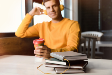 Man with headphones connected to book at table in cafe