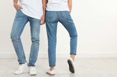 Photo of Young couple in stylish jeans near white wall, closeup