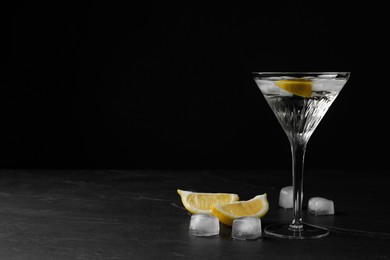 Photo of Martini glass of refreshing cocktail with lemon and ice cubes on black textured table. Space for text