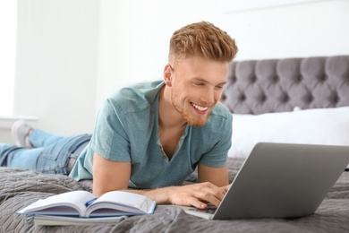 Young man using laptop while lying on bed at home