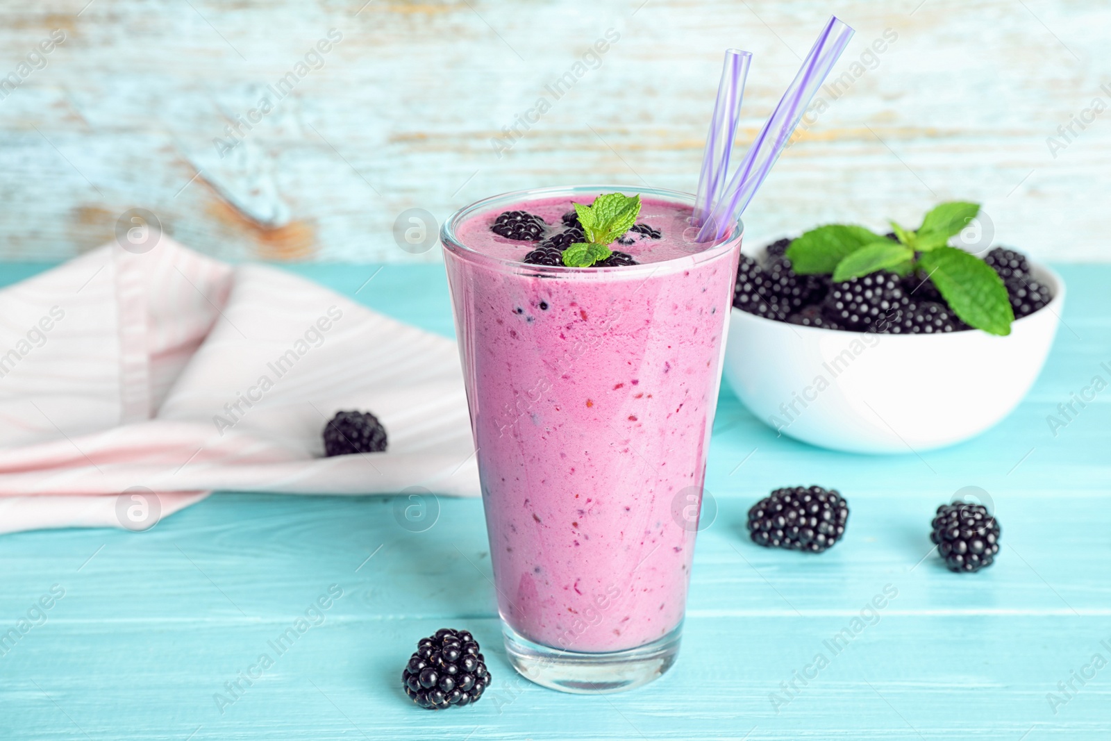 Photo of Delicious blackberry smoothie in glass on light blue wooden table