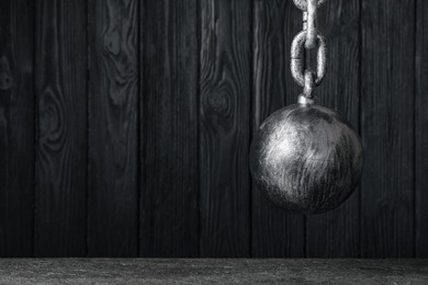 Photo of Prisoner ball with chain hanging near black wooden wall, space for text