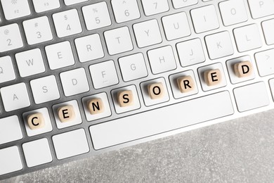 Photo of Wooden cubes with word Censored and keyboard on light grey table, top view