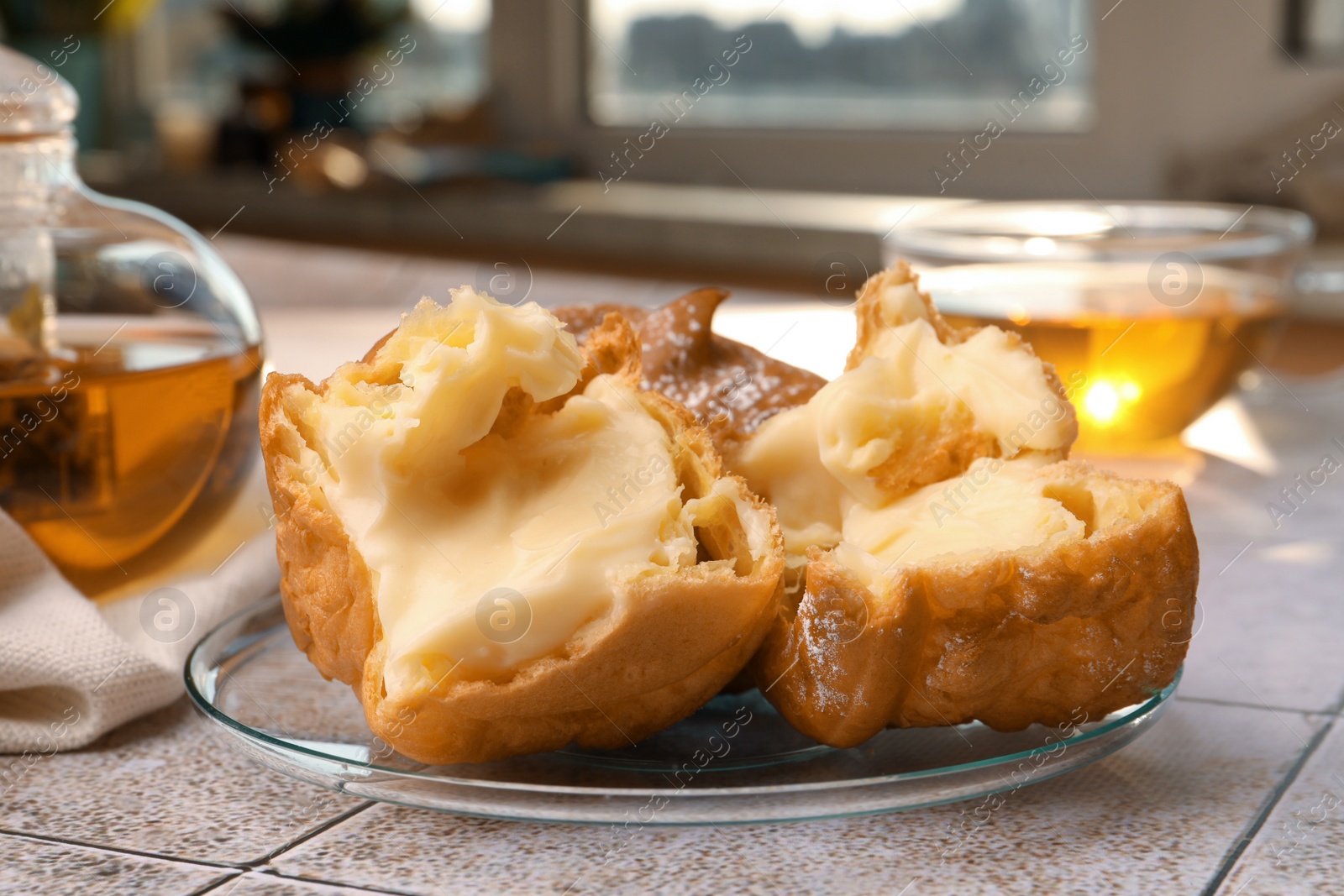 Photo of Delicious profiteroles filled with cream and tea on white tiled table, closeup