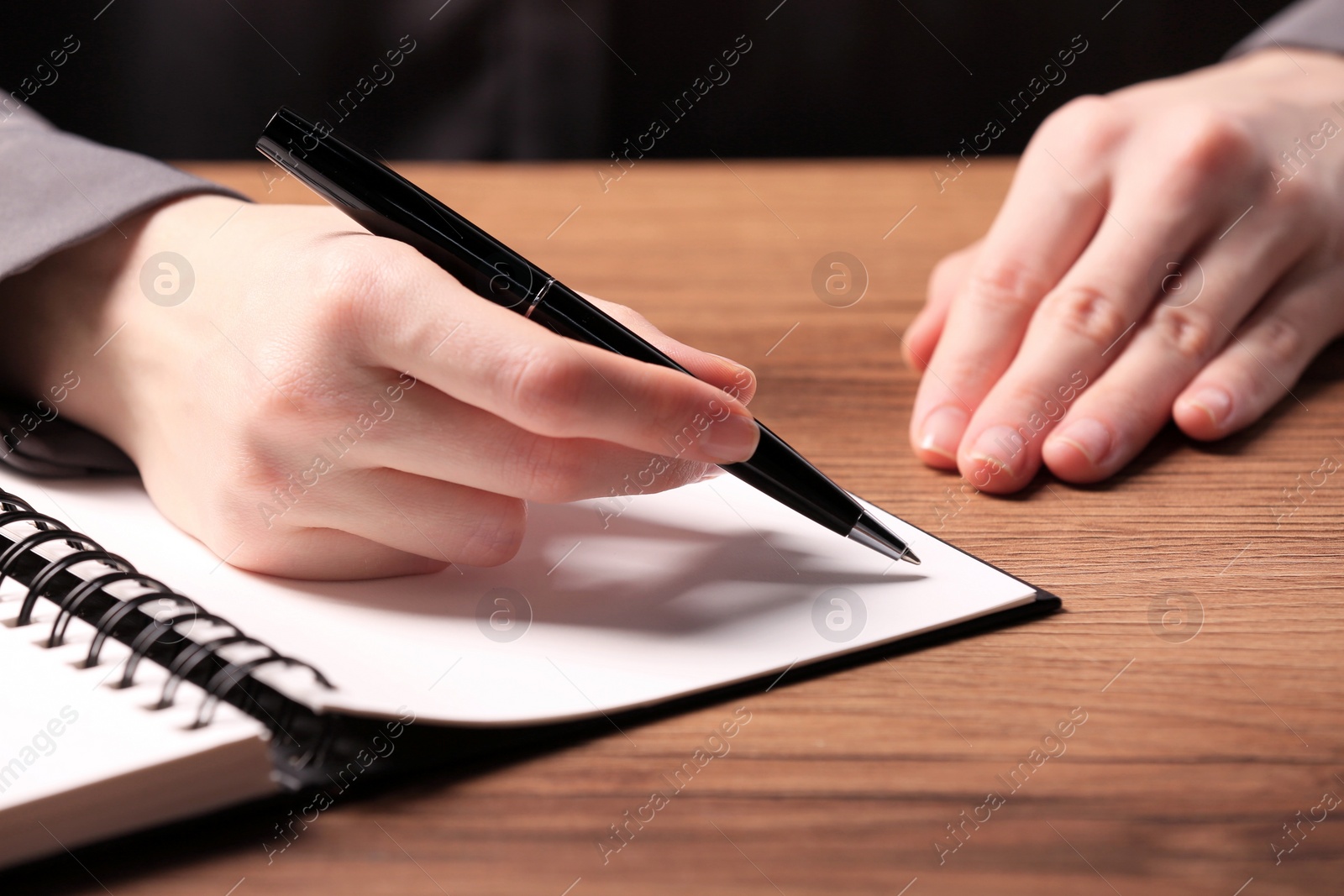 Photo of Woman writing in notebook at wooden table, closeup