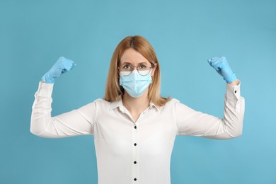 Photo of Woman with protective mask and gloves showing muscles on light blue background. Strong immunity concept