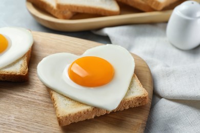 Photo of Heart shaped fried egg and toast on wooden board, closeup