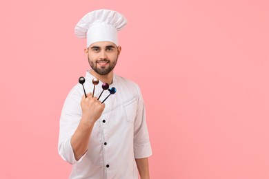 Photo of Professional chef holding kitchen utensils on pink background. Space for text