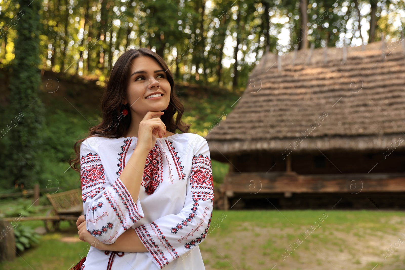 Photo of Beautiful woman wearing embroidered shirt in village, space for text. Ukrainian national clothes