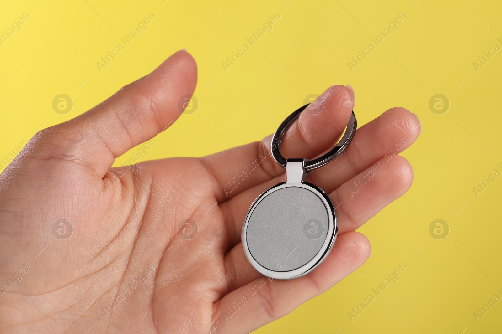 Photo of Woman holding metallic keychain on yellow background, closeup