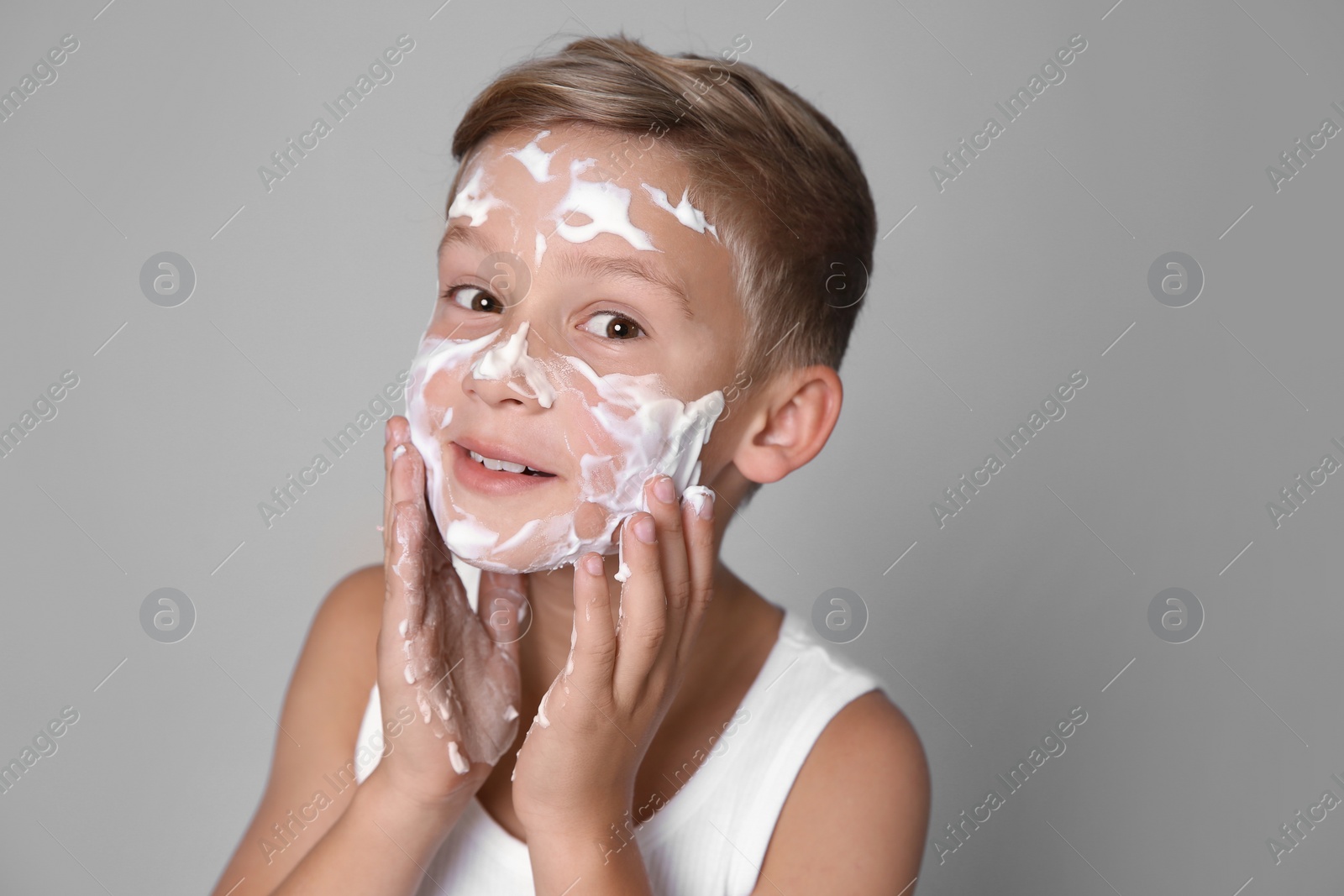 Photo of Cute little boy with soap foam on face against gray background