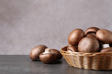 Photo of Wicker bowl and fresh champignon mushrooms on table against color background. Space for text