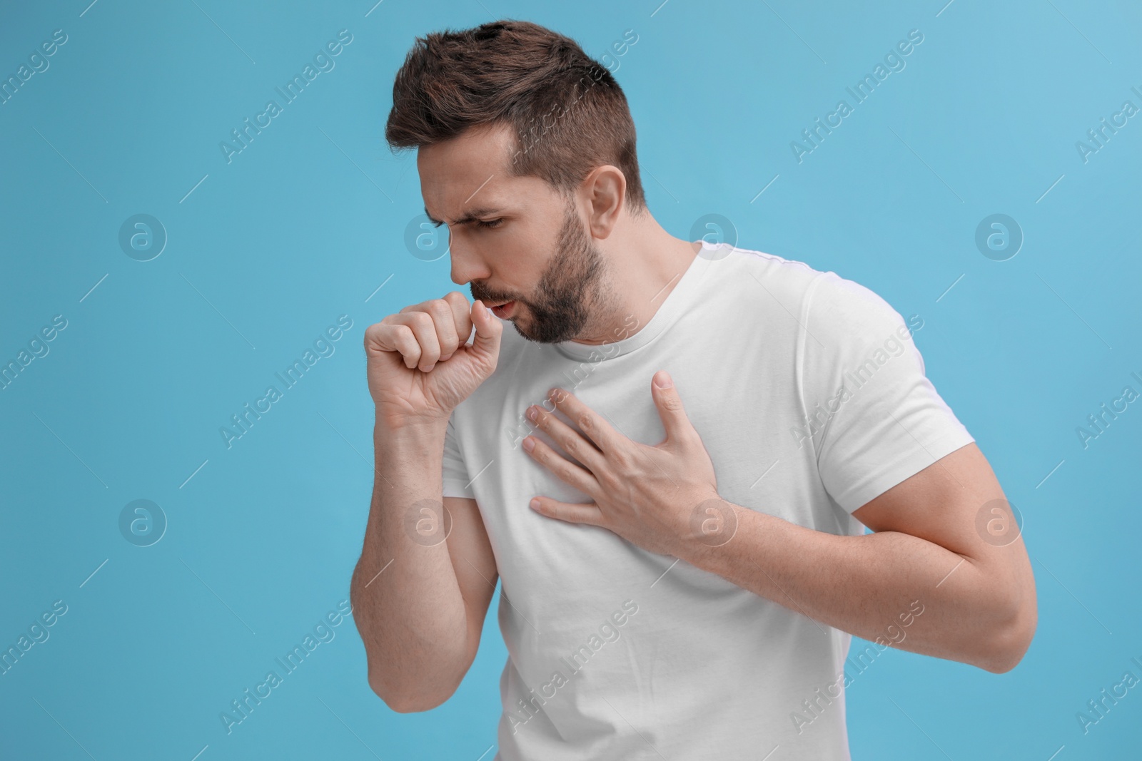 Photo of Man coughing on light blue background. Cold symptoms