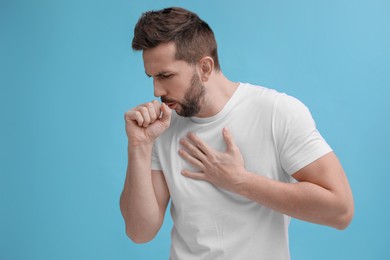 Photo of Man coughing on light blue background. Cold symptoms