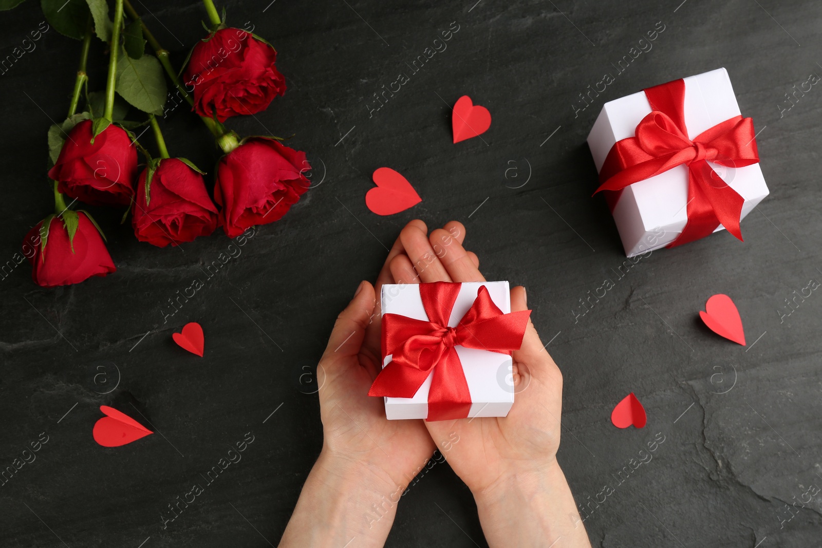 Photo of Woman holding gift box at black table, top view. Valentine's Day celebration