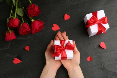 Photo of Woman holding gift box at black table, top view. Valentine's Day celebration
