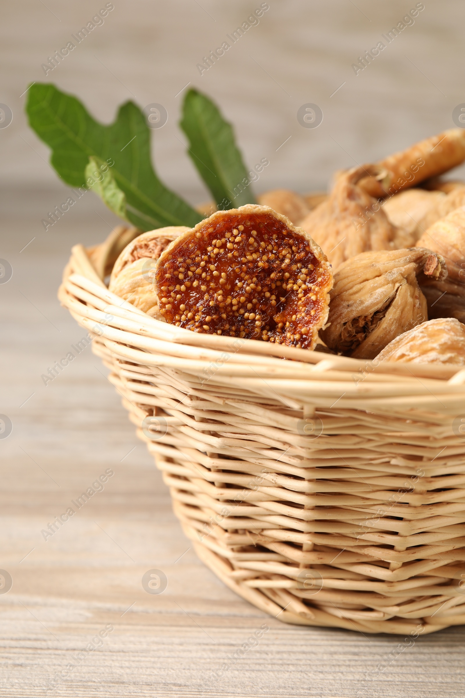 Photo of Wicker basket with tasty dried figs and green leaf on light wooden table, closeup