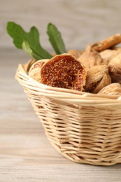Wicker basket with tasty dried figs and green leaf on light wooden table, closeup