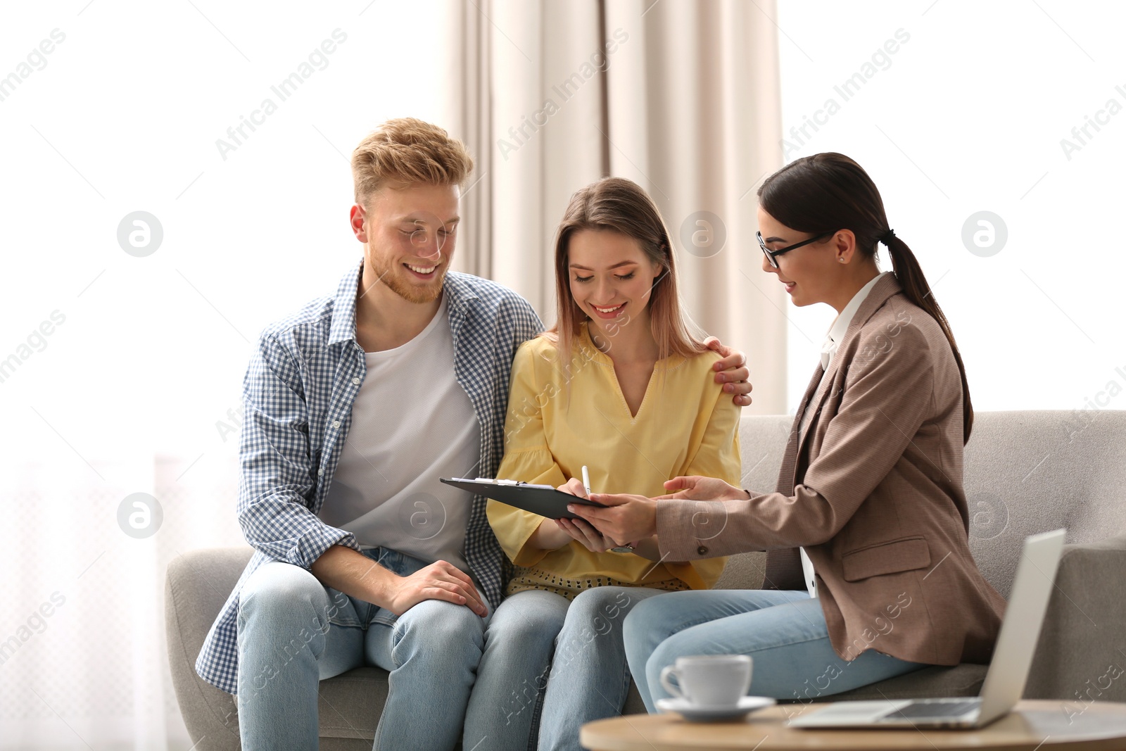 Photo of Young couple signing contract with female insurance agent in office