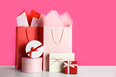 Photo of Gift bags and boxes on white table against pink background