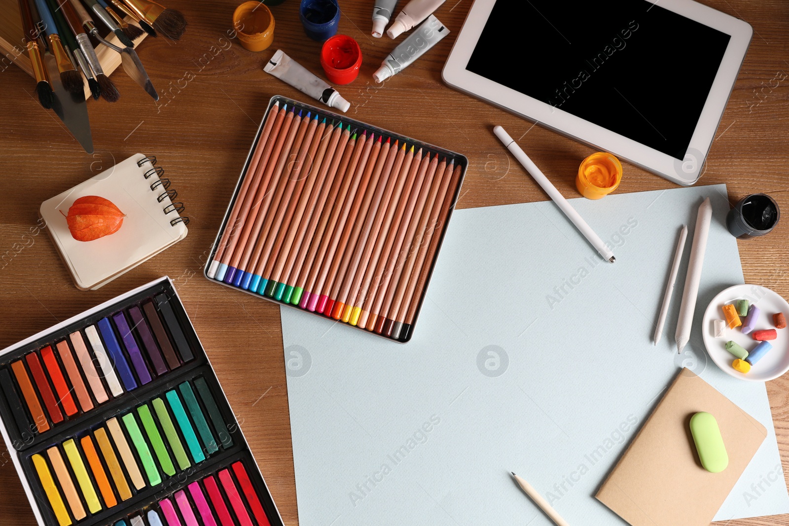 Photo of Artist's workplace with tablet, soft pastels and drawing pencils on table, flat lay