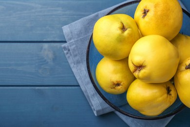 Tasty ripe quinces in bowl on blue wooden table, top view. Space for text