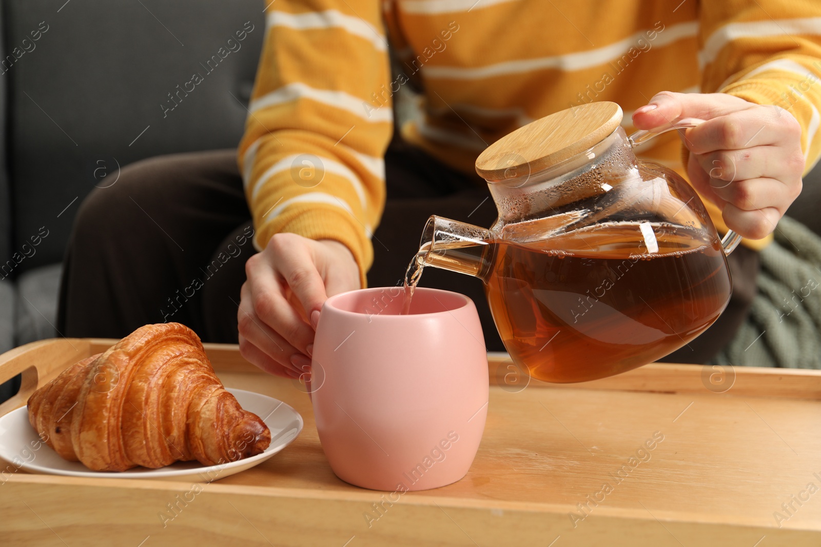 Photo of Woman pouring aromatic tea into cup at table, closeup