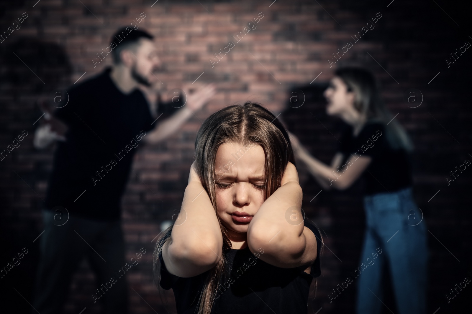 Photo of Scared little girl and blurred view of quarrelling parents on background. Domestic violence